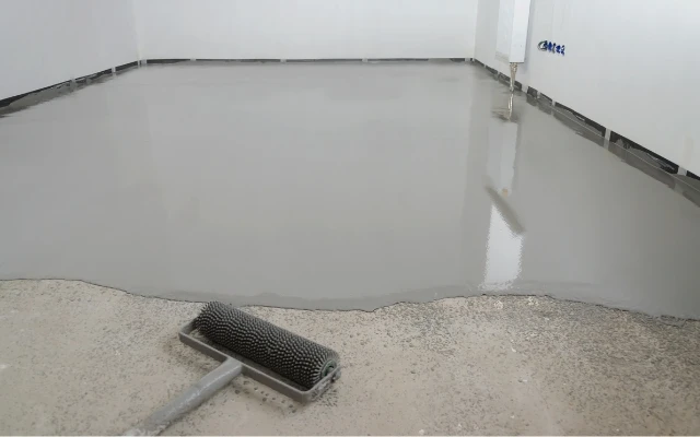 Světle šedá podlahová směs s válcem na betonovém základu.