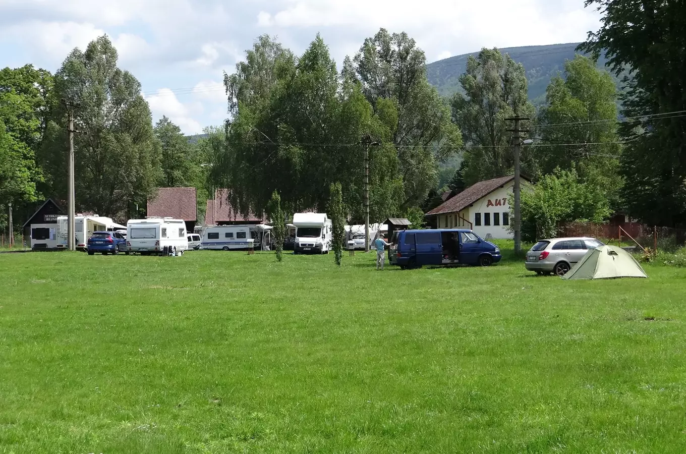 Autokemp v Hejnicích s karavany, stany a vozidly na trávníku.