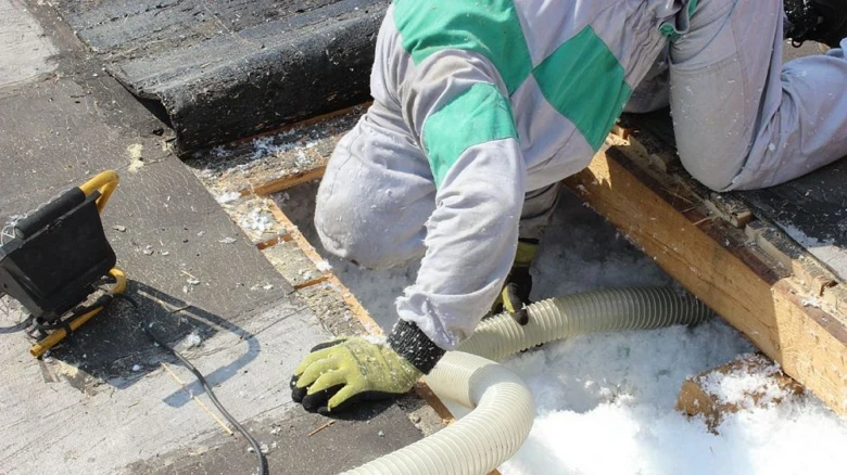 Stavebník fouká izolační materiál do střešní konstrukce.