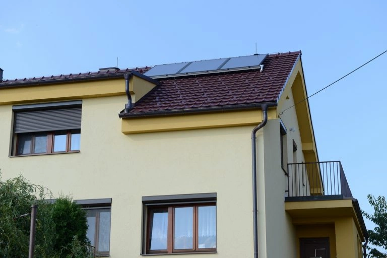 Žlutý dům s tmavou střechou a solárními panely na střeše.