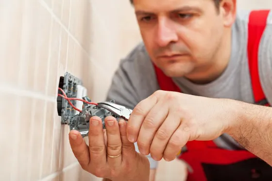 Elektrikář zapojuje dráty do elektrické zásuvky v zdi.