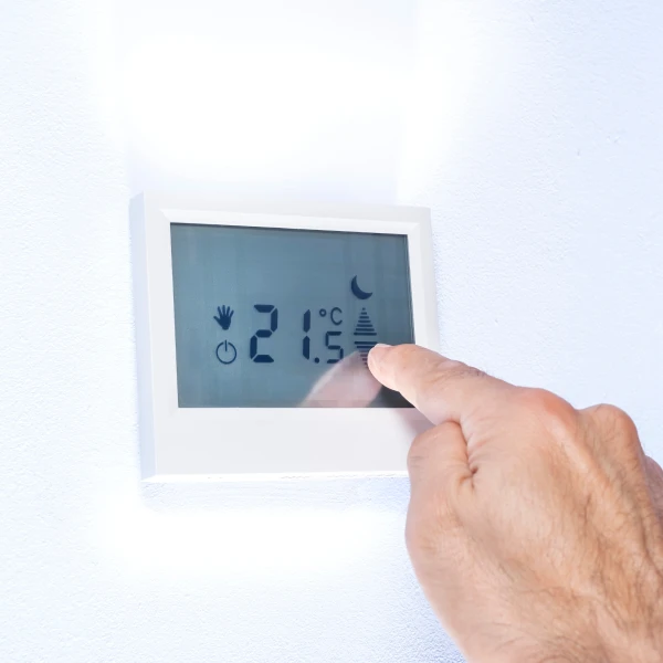 Ruka nastavuje teplotu na digitálním termostatu pro úsporu energie.