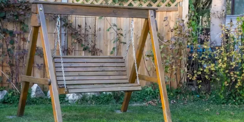 Hotová dřevěná houpačka na zahradu visící ze železných řetězů.