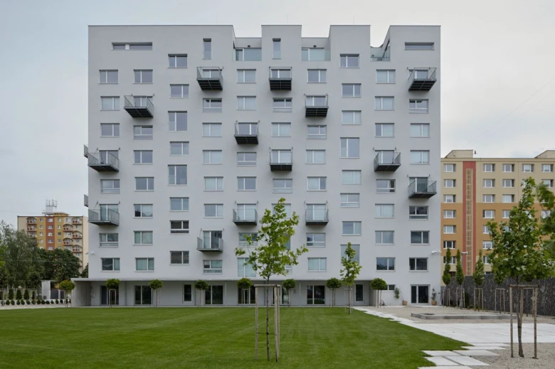 Moderní bílý panelák s balkóny před zelenou travnatou plochou.