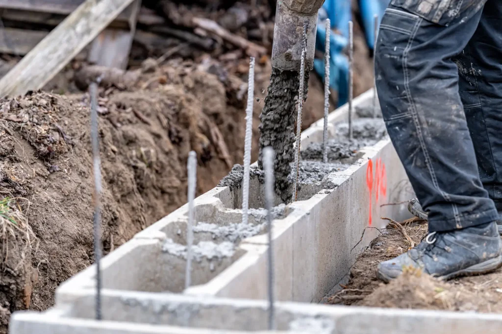 Stavebník nalévá beton do bednění s výztuží pro plot.