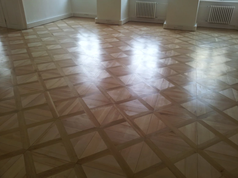 Lesklá parketová podlaha s geometrickým vzorem po renovaci.