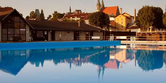 Venkovní bazén v Kroměříži s odrazem města ve vodě.