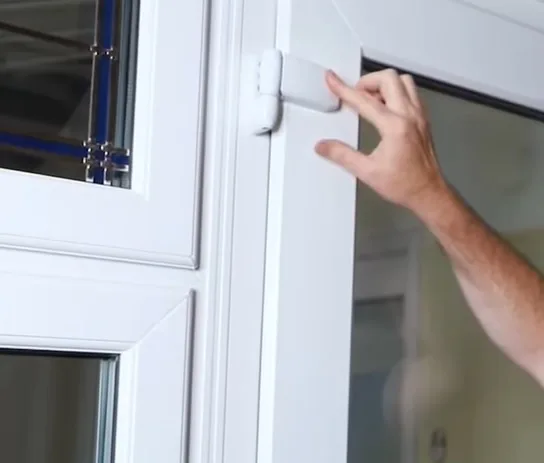 Ruka nastavuje zámek na plastovém okně nebo dveřích.