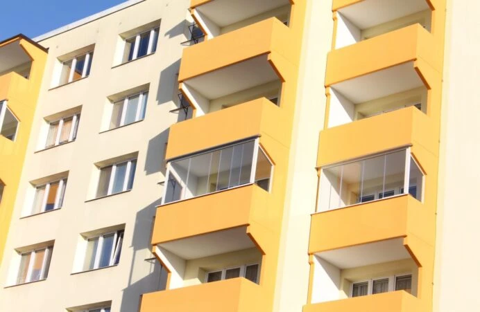 Zasklené balkony na fasádě bytového domu s oranžovými prvky.