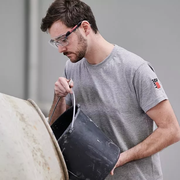 Muž nalévá beton z kbelíku do míchací nádoby.