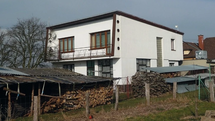 Moderní bílý dům s dřevěným ohništěm na pozadí.