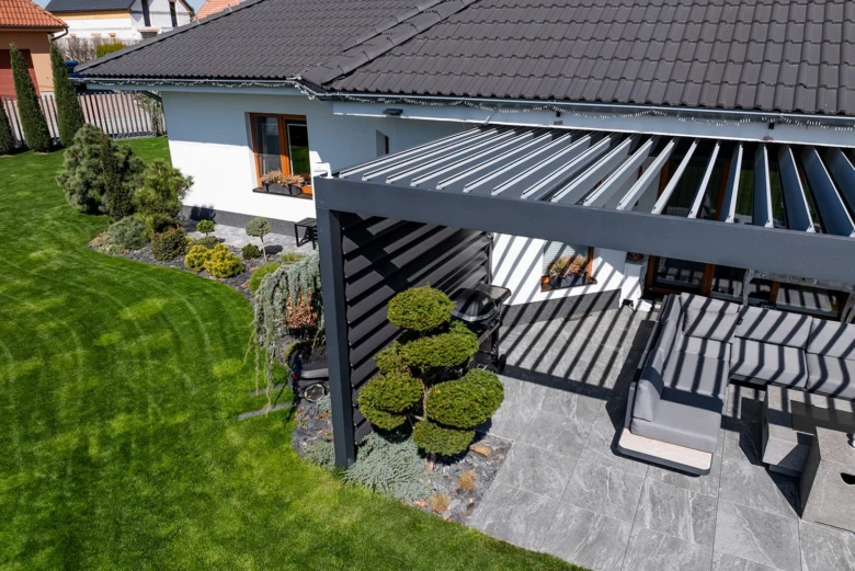 Moderní šedá kovová pergola u bílého domu s zahradou.