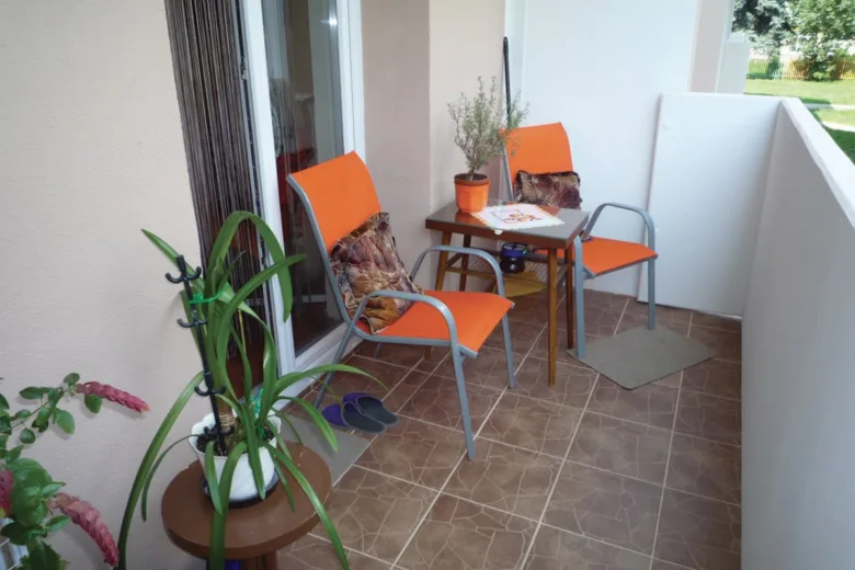 Přestavěná lodžie s oranžovými židlemi, stolkem a rostlinami.