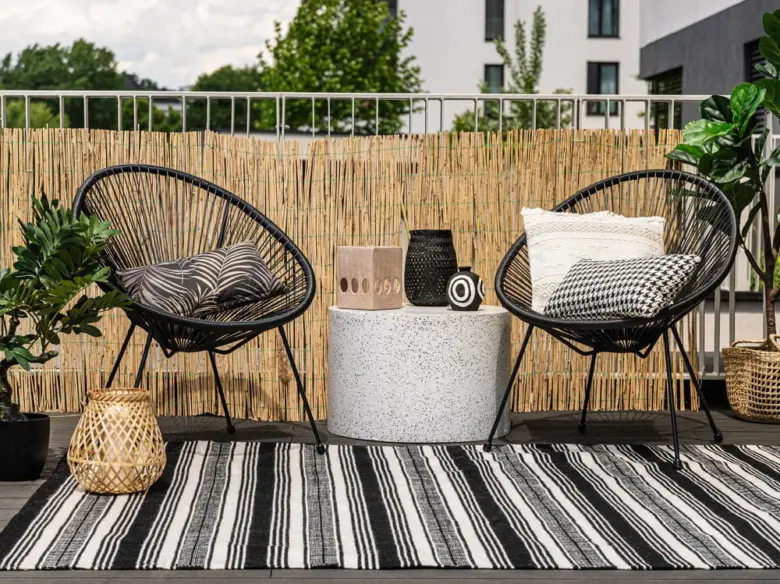 Černobílý pruhovaný koberec na balkóně s židlemi a rostlinami.