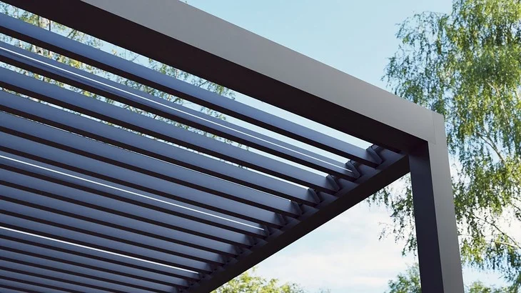 Moderní tmavá bioklimatická pergola s lamelami pod modrou oblohou.