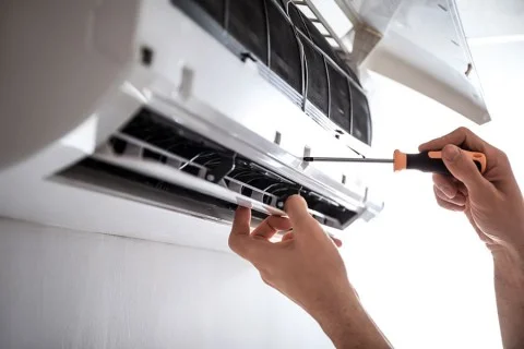 Technik opravuje klimatizaci v domácnosti pomocí šroubováku.