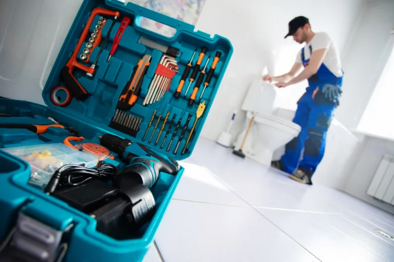 Plumber working on leaking toilet with open tool kit nearby.