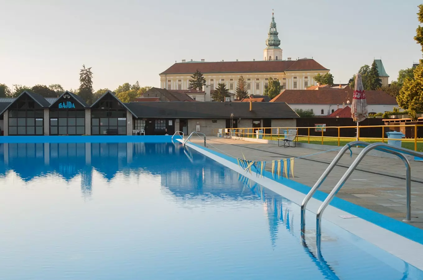 Venkovní bazén v Kroměříži s historickým kostelem na pozadí.