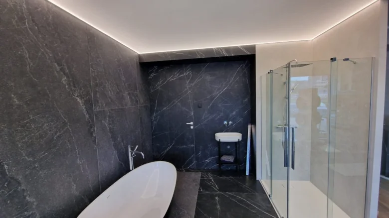 Moderní koupelna s velkoformátovou tmavou dlažbou na stěnách i podlaze.