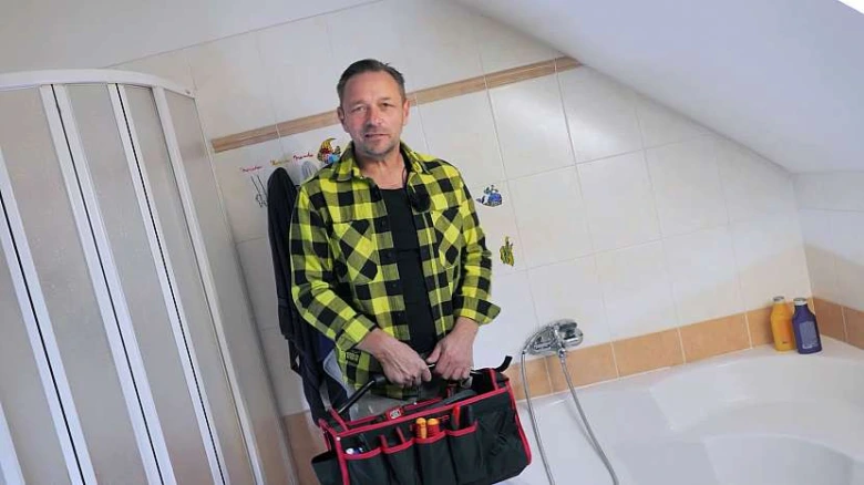 Muž s nářadím v koupelně u sprchového přepínače