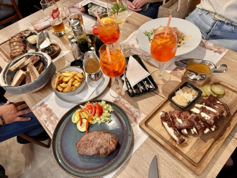 Stůl v restauraci s jídlem jako steaky, bramborami a koktejly.