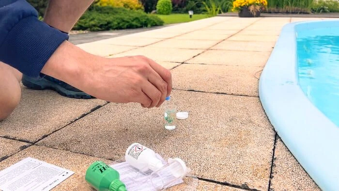 Ruka drží láhev s chemií pro kontrolu vody v bazénu.