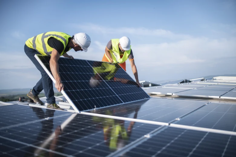 Dva dělníci montují fotovoltaický panel na střechu.
