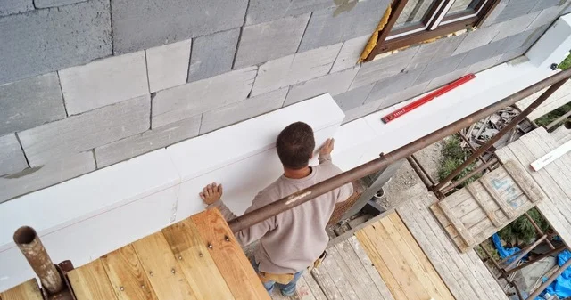 Stavebník kotví polystyrénovou desku na fasádu pomocí lepidla a skrutky.