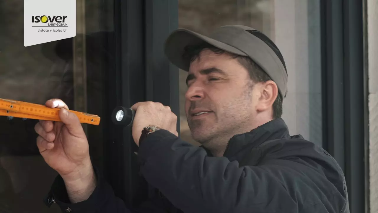 Muž kontroluje kotvení styroporu na fasádě pomocí nástroje.