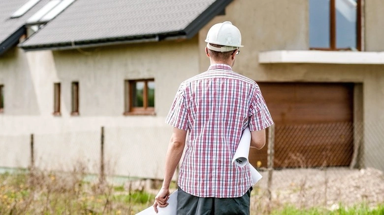 Architekt s plány stojí před domem v rekonstrukci.