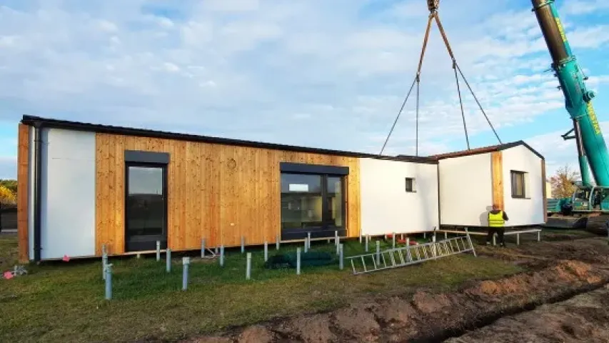 Modulová dřevostavba je zvedána kranem na staveništi.
