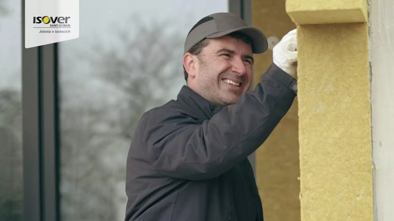 Muž instaluje žlutou minerální vlnu na fasádu domu.