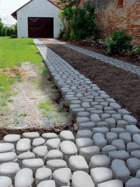 Nová cesta z betonových zatravňovacích kostek vedle trávníku.