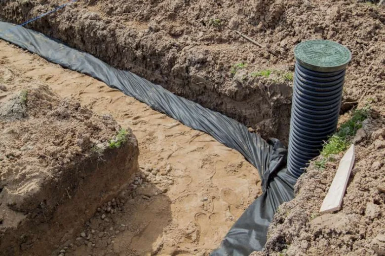 Instalace odvodňovacího systému s drenážním potrubím v příkopu.