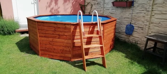 Dřevěné obložení nadzemního bazénu na trávníku s žebříkem.