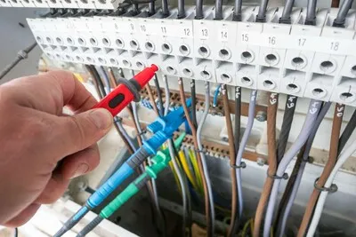 Ruční kontrola elektrické instalace pomocí měřicího nástroje v rozvaděči.
