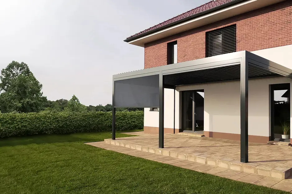 Bioklimatická pergola s roletami na terase u domu v zelené zahradě.