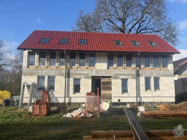 Rodinný dům v hrubé stavbě s červenou střechou na pozadí modrého nebe.