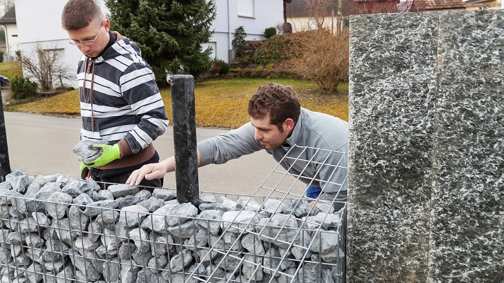 Muži plní drátěné koše kameny pro zahradní gabionovou zeď.