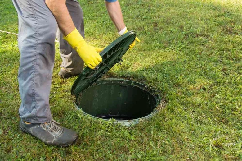 Pracovník odemyká víko septické nádrže na trávníku.