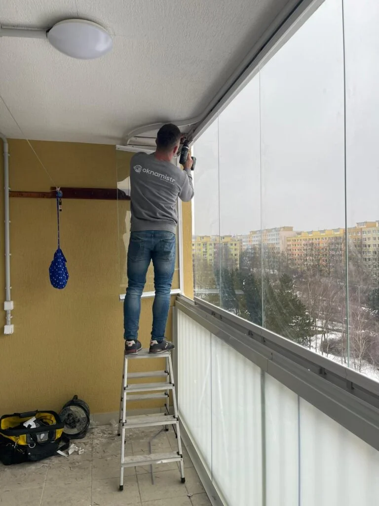 Montáž skla na balkoně - dělník instaluje zasklení balkonu.