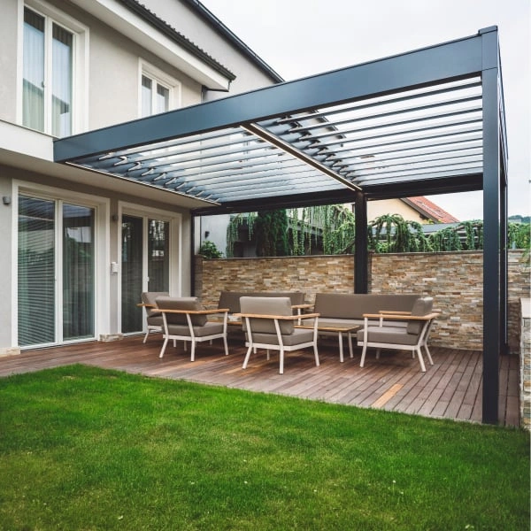 Moderní černá pergola na dřevěné terase u domu s kamennou zdí.