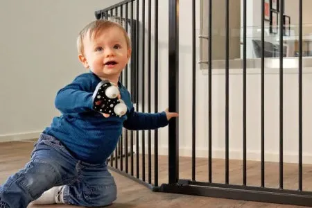 Malý dítě drží černou bezpečnostní zábranu u dveří.