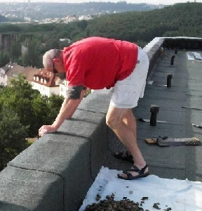 Muž pracuje na atice střechy bytového domu.