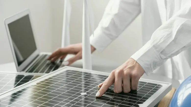 Vědecký pracovník ukazuje na fotovoltaickou desku při práci s notebookem.