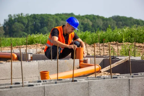 Stavebník montuje oranžové potrubí do betonového základu s výztuhami