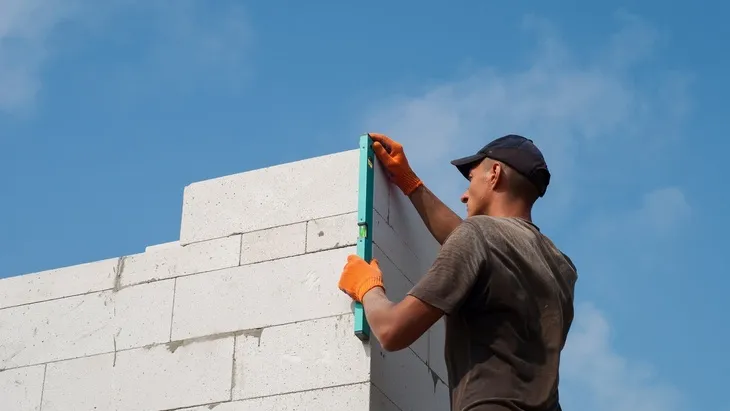 Stavebník kontroluje svislost betonových bloků pomocí vodováhy.