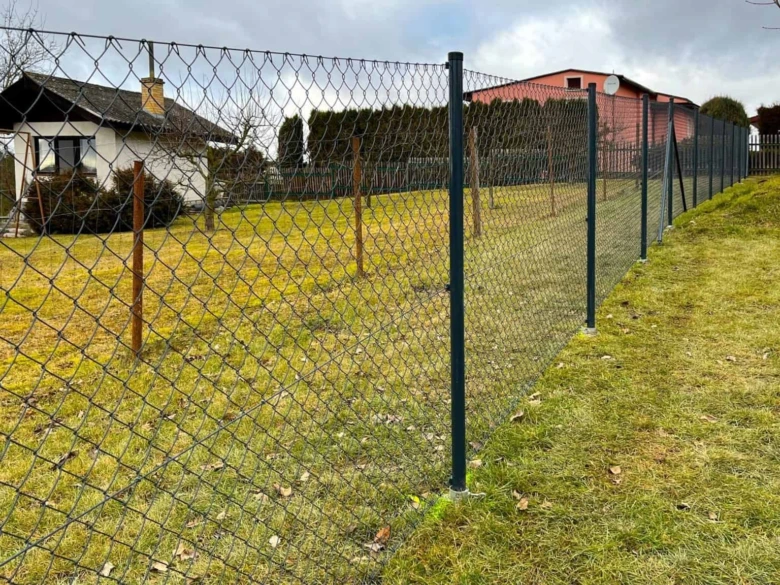 Ocelová plot s drátěnou mříží kolem domu na trávníku.