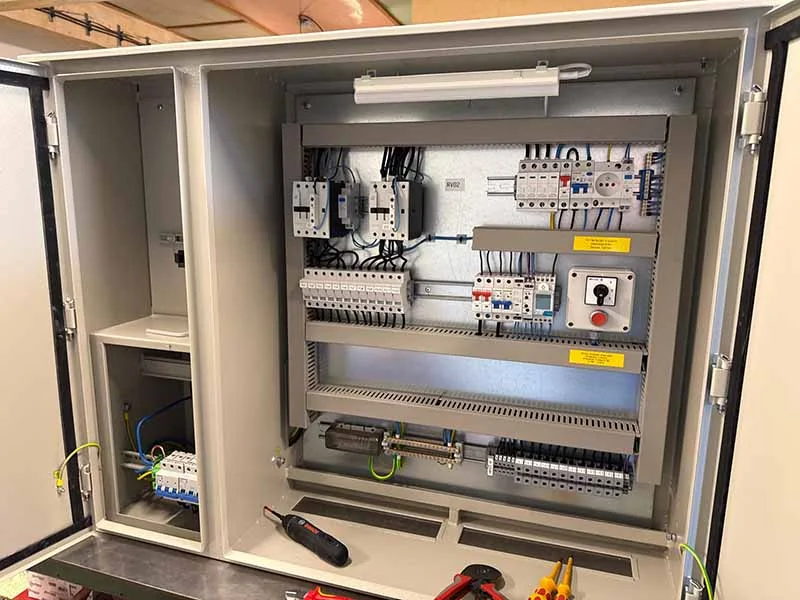 Otevřený průmyslový elektrický rozvaděč s komponenty a nástroji.
