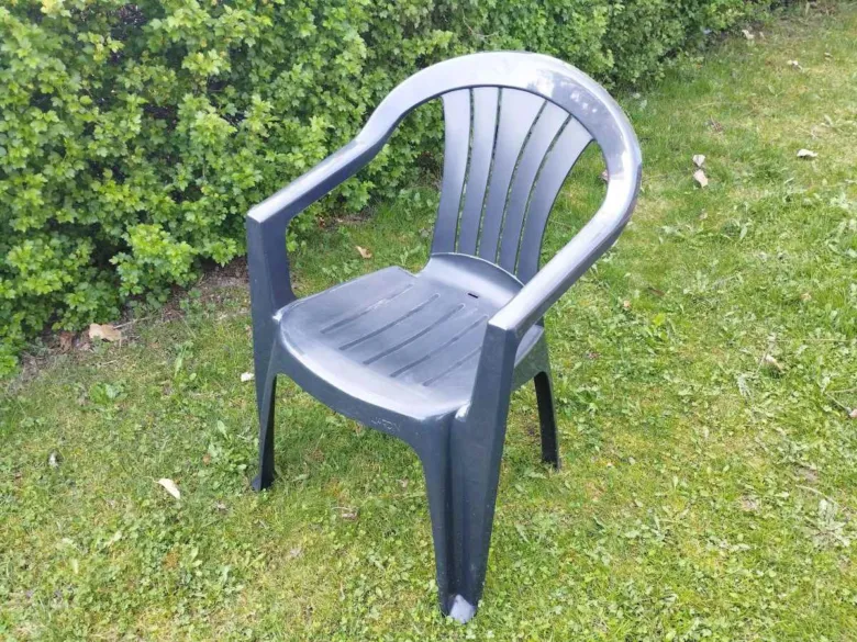 Tmavé plastové zahradní křeslo na trávě u keře.